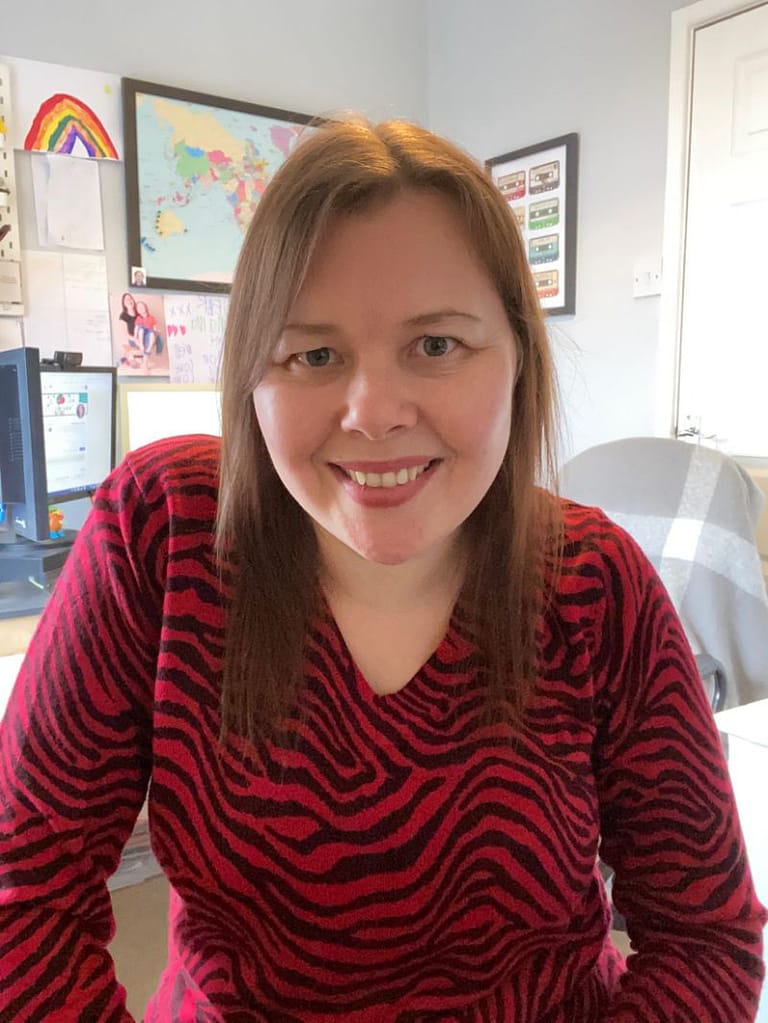 Louisa wearing a red and black stripy top sitting in her office.